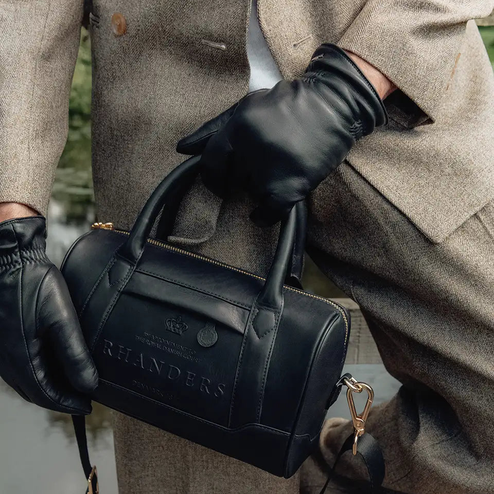 The Crown Handbag from RHANDERS is lined with heritage RH Monogram logo, has inside and outside pockets, and is adorned with an adjustable Kalmus embossed leather and textile strap.