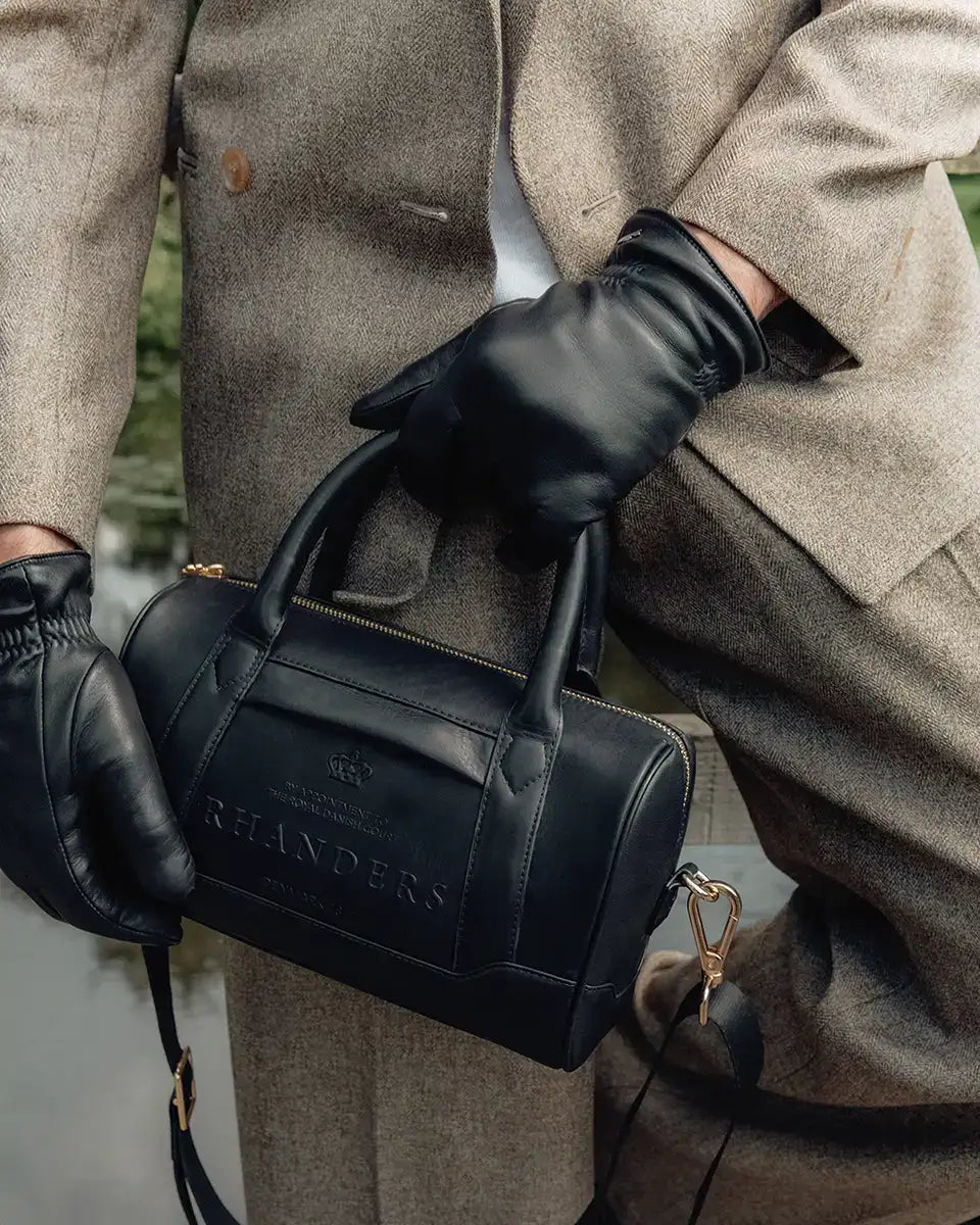 The Crown Handbag from RHANDERS is lined with heritage RH Monogram logo, has inside and outside pockets, and is adorned with an adjustable Kalmus embossed leather and textile strap.