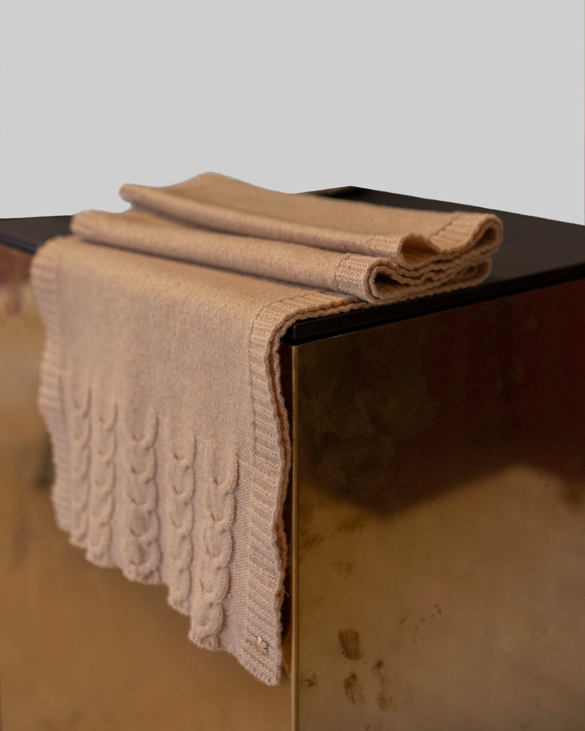 The Arie Scarf in the colour camel adorned with knitted details and a 14 karat gold-plated Kalmus flower in one corner.