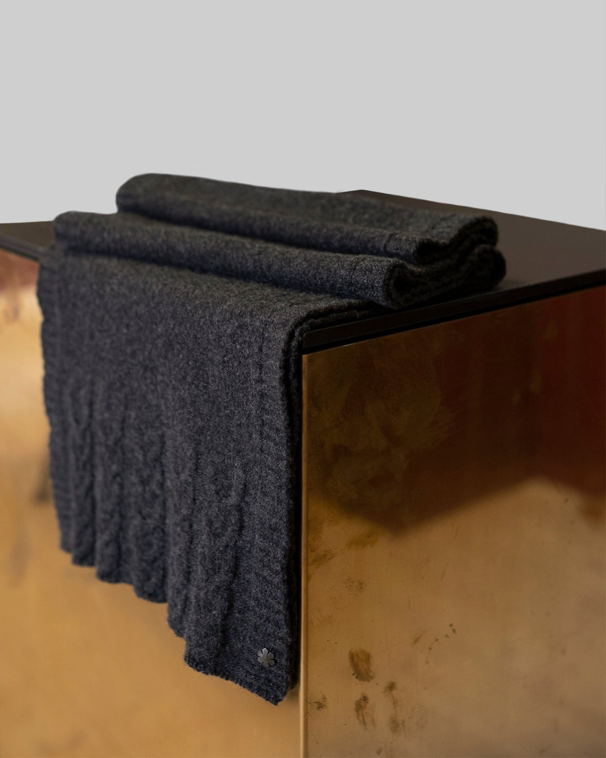 Arie Tørklædet i farven koksgrå prydet med strikkede detaljer og en hæmatitbelagt Kalmus blomst i det ene hjørne.