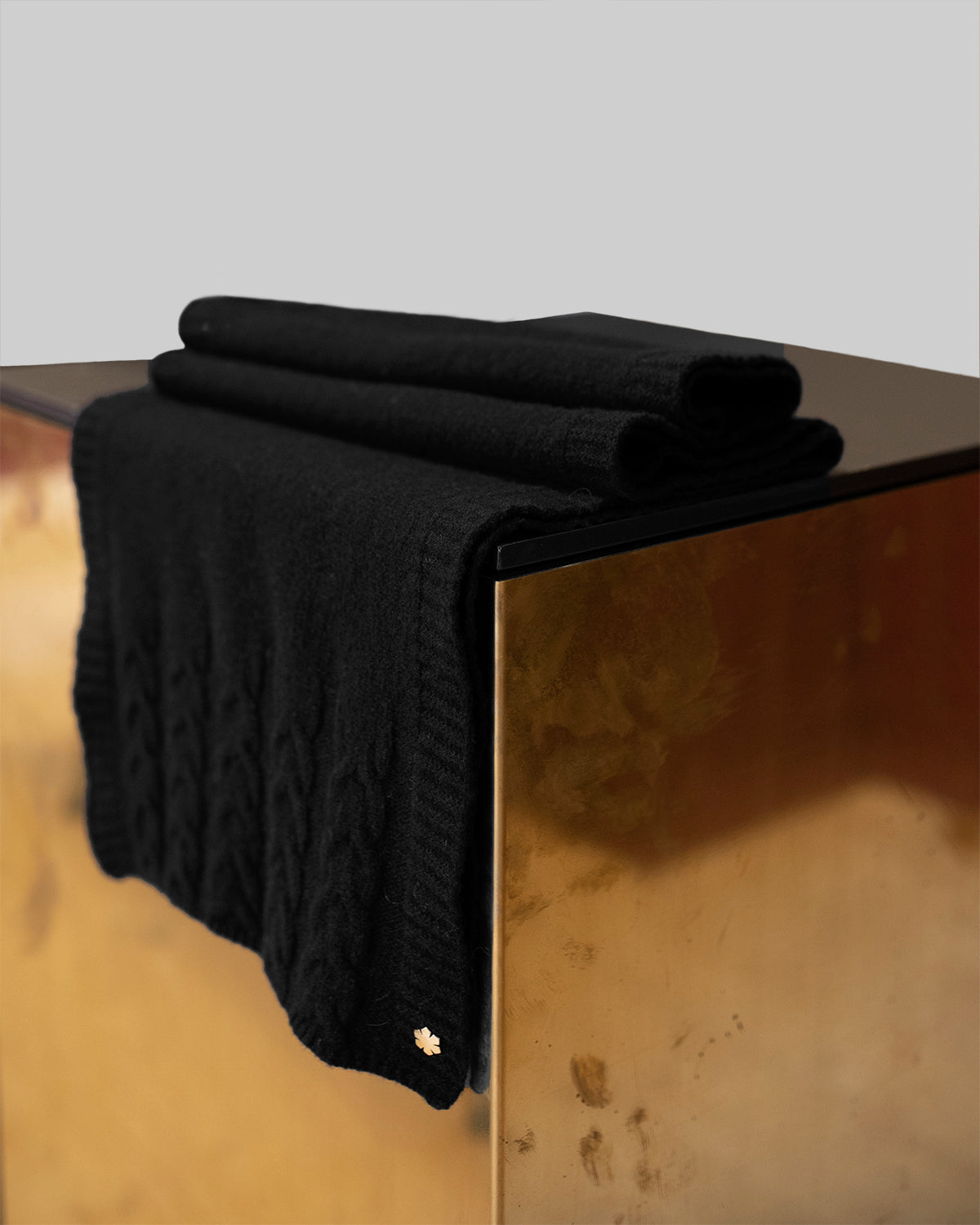 Sort Arie Tørklæde prydet med strikkede detaljer og en 14 karat forgyldt Kalmus blomst i det ene hjørne.