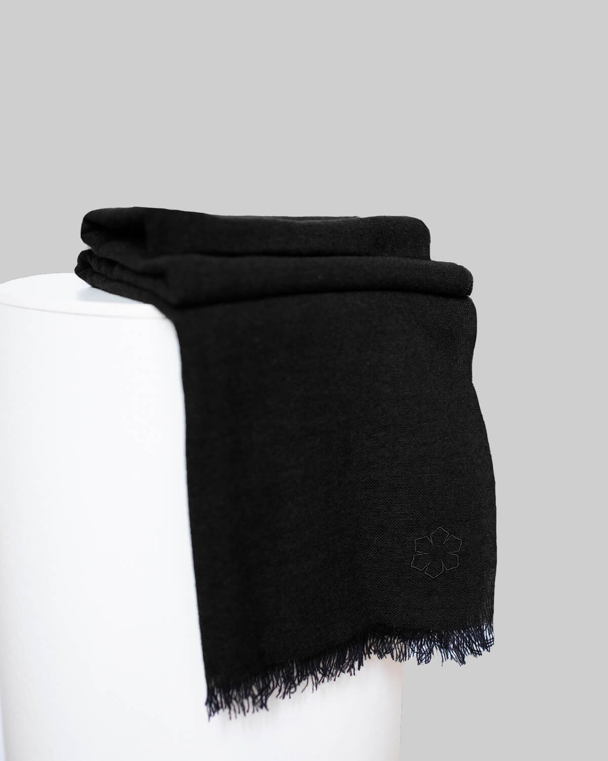 Black Aston Scarf adorned with an embroidered outline Kalmus flower in one corner.