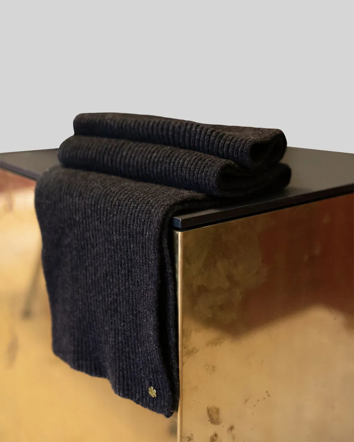 Male Alex Scarf in the colour charcoal adorned with a gold-pleated Kalmus-flower in one corner.